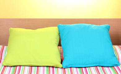 bright pillows on bed on yellow background