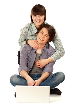A couple sitting on the floor behind a laptop, isolated on white