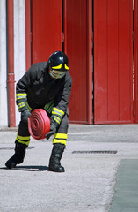 Fototapeta premium Fireman while unrolls a fire hose to extinguish the flames