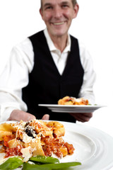 A waiter serves pasta. Focus on plate. Close-up.