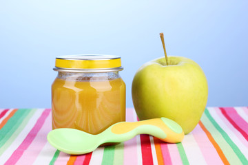 Jar of baby puree with spoon on napkin on blue background