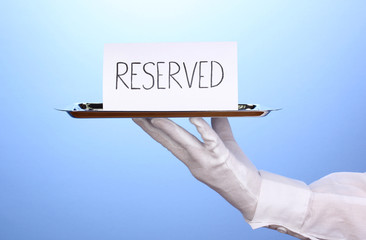 Hand in glove holding silver tray with card saying reserved