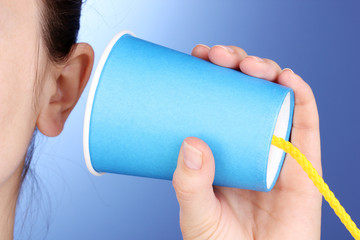 Human ear and paper cup near it close-up on blue background
