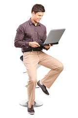 Young man sitiing on a stool and working on a laptop
