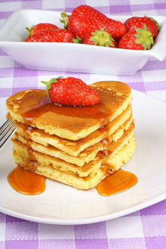 Stack of heart-shaped pancakes with syrup and strawberry