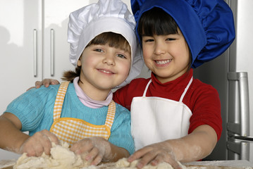Dos niñas cocinando masa y pizza en una cocina.