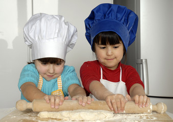 Dos niñas cocinando masa y pizza en una cocina.
