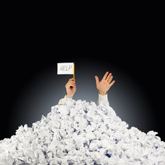 Person under crumpled pile of papers with hand holding a help si