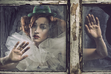 A lonely sad pierrot woman behind the glass