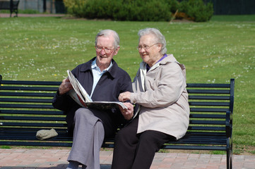Senior couple reading a newspaper on a park bench