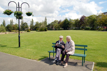 Senior couple reading a newspaper on a park bench