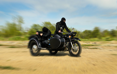 Two armed men riding a motorcycle with a sidecar. Motion blur.