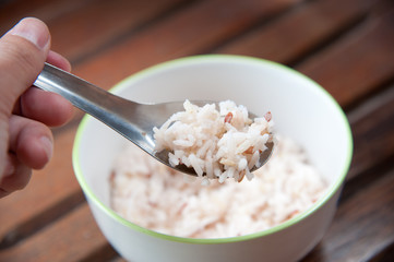 White and brown steamed rice with spoon in white round bowl