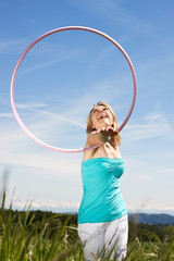 Blonde Frau drehtt rosa Hula Hoop Reifen um den Arm