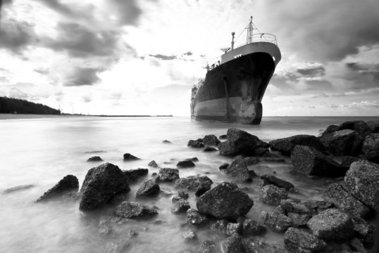 Fototapeta Cargo ship run aground on rocky shore shore, black and white