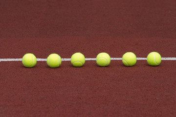 Yellow tennis balls in-line on court with synthetic surface