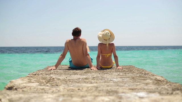 Couple sitting on beautiful stone pier by tropical sea