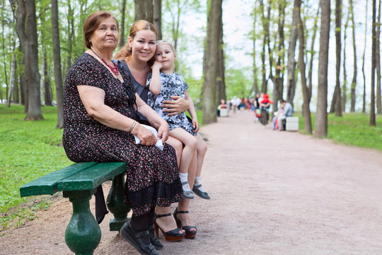 Three Women Different Ages Are Sitting On Bench In Park