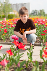 The boy sitting next to the flowerbed with tulips