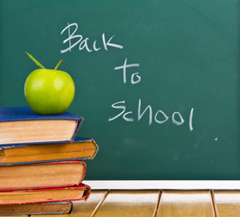 Back to school written on chalkboard with green apple and books