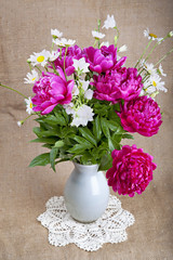 Bouquet of peonies and daisies in a white vase on a lace napkin