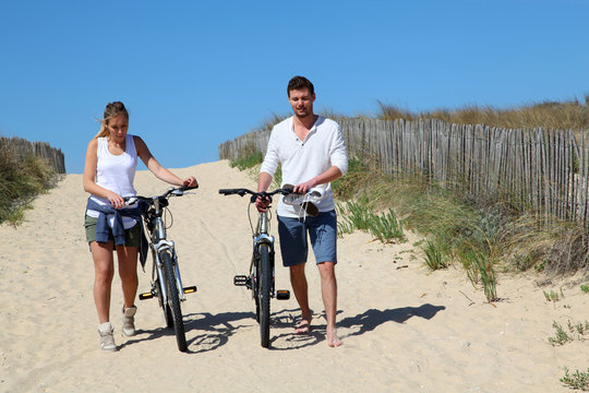 Couple walking on a sandy path with bicycles