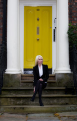 Beautiful young woman sat on steps in front of yellow door