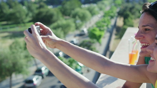 Female friends taking photo with cellphone on balcony