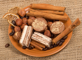 Sweets, cinnamon, nuts and coffee beans on a saucer, on burlap b