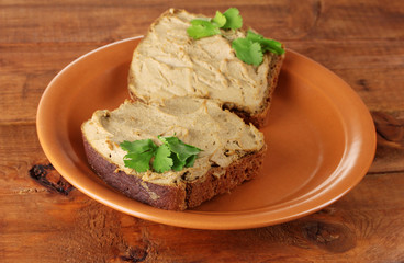 Fresh pate on bread on brown plate on wooden table