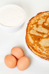 Pile of pancakes with some flour and eggs on white background