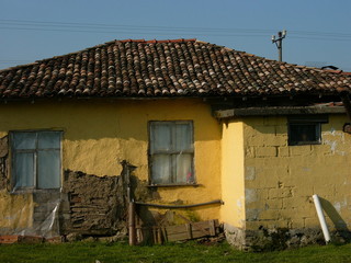 assade in Beige und Ocker eines alten Haus mit traditionellem Ziegeldach vor blauem Himmel im...