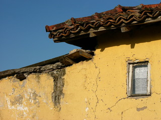 Bröckelnde Fassade eines Lehmhaus in Beige und Ocker vor blauem Himmel im Sonnenschein im Dorf...