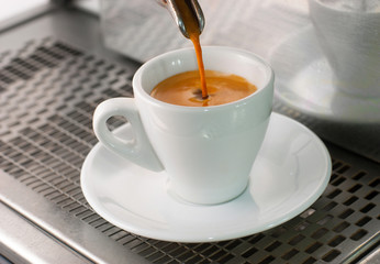 Espresso pours out of a group head into a coffee shot glass.