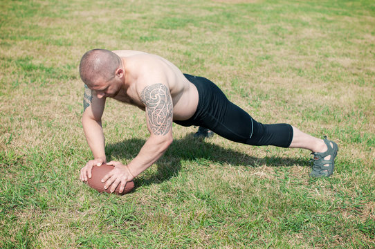 Shirtless male athlete doing push ups with american football