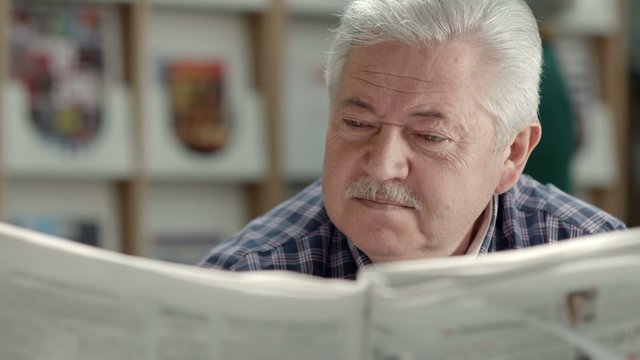 Senior man with mustache reading newspaper in library