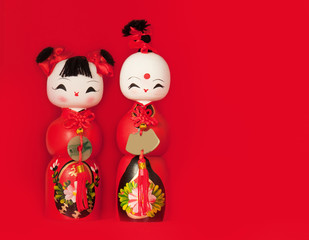 Two traditional wooden Chinese dolls against red background