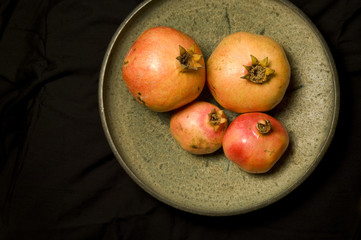 four pomegranates in a bowl, black background