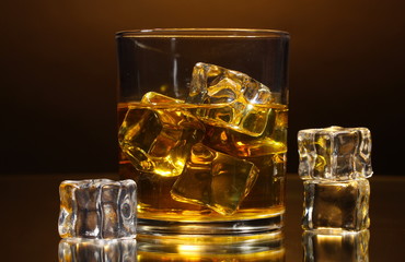 glass of whiskey and ice on brown background
