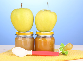 Jars of baby puree with spoon on napkin on blue background