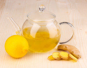 Healthy ginger tea in kettle with lemon on wooden background
