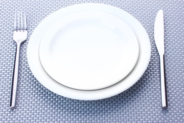 White empty plates with fork and knife on a grey tablecloth