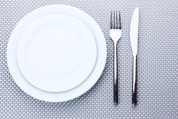 White empty plates with fork and knife on a grey tablecloth
