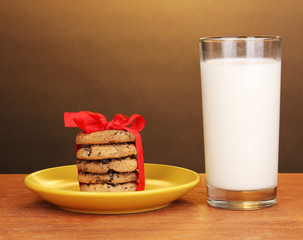 Glass of milk and cookies on wooden table on brown background