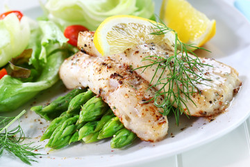 Fried fish on green asparagus with salad