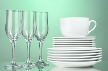 Clean plates, cup and glasses on green background
