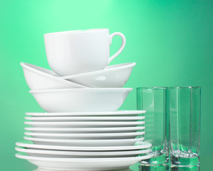 Clean plates, cup and glasses on green background