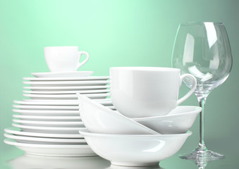 Clean plates, cups and glasses on green background