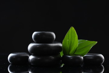 Obraz premium Spa stones and green leaves on black background