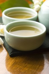 Obraz na płótnie Canvas Zielona herbata z jaśminem w filiżance i czajniczek na drewnianym stole